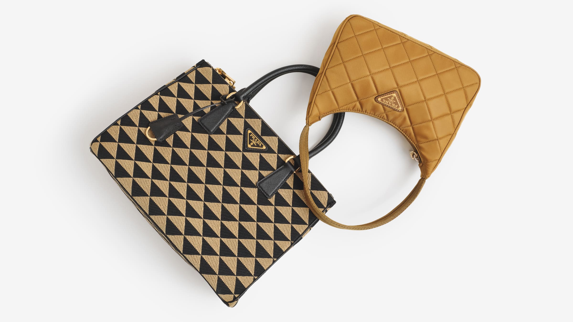 A Prada Jacquard Saffiano Triangolo Symbole Embroidered Large Double Zip Tote in Black Corda and a Prada Tessuto Nylon Stitched Shoulder Bag in Tobacco laying flat at angle.