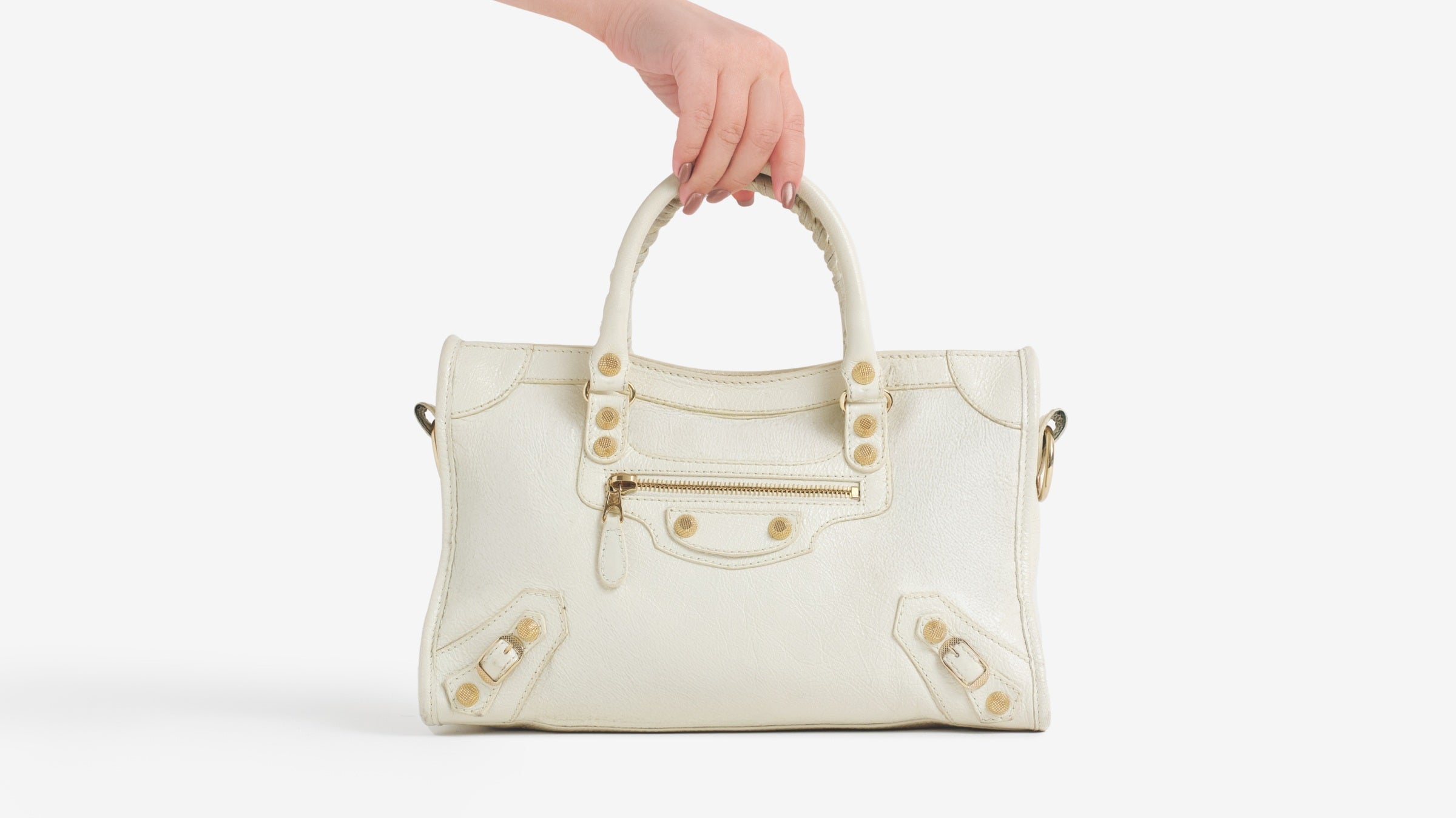 A hand holds the top handle of a Agneau Giant 12 Rose Gold Hardware City White Light