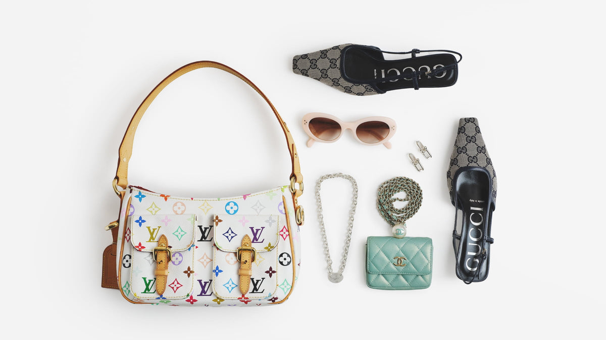 Flat lay arrangement of luxury accessories on a white background, featuring a white multicolored Louis Vuitton shoulder bag, a mint green Chanel micro bag, grey and black monogrammed Gucci slingback heels, pink Celine sunglasses, and silver jewelry.