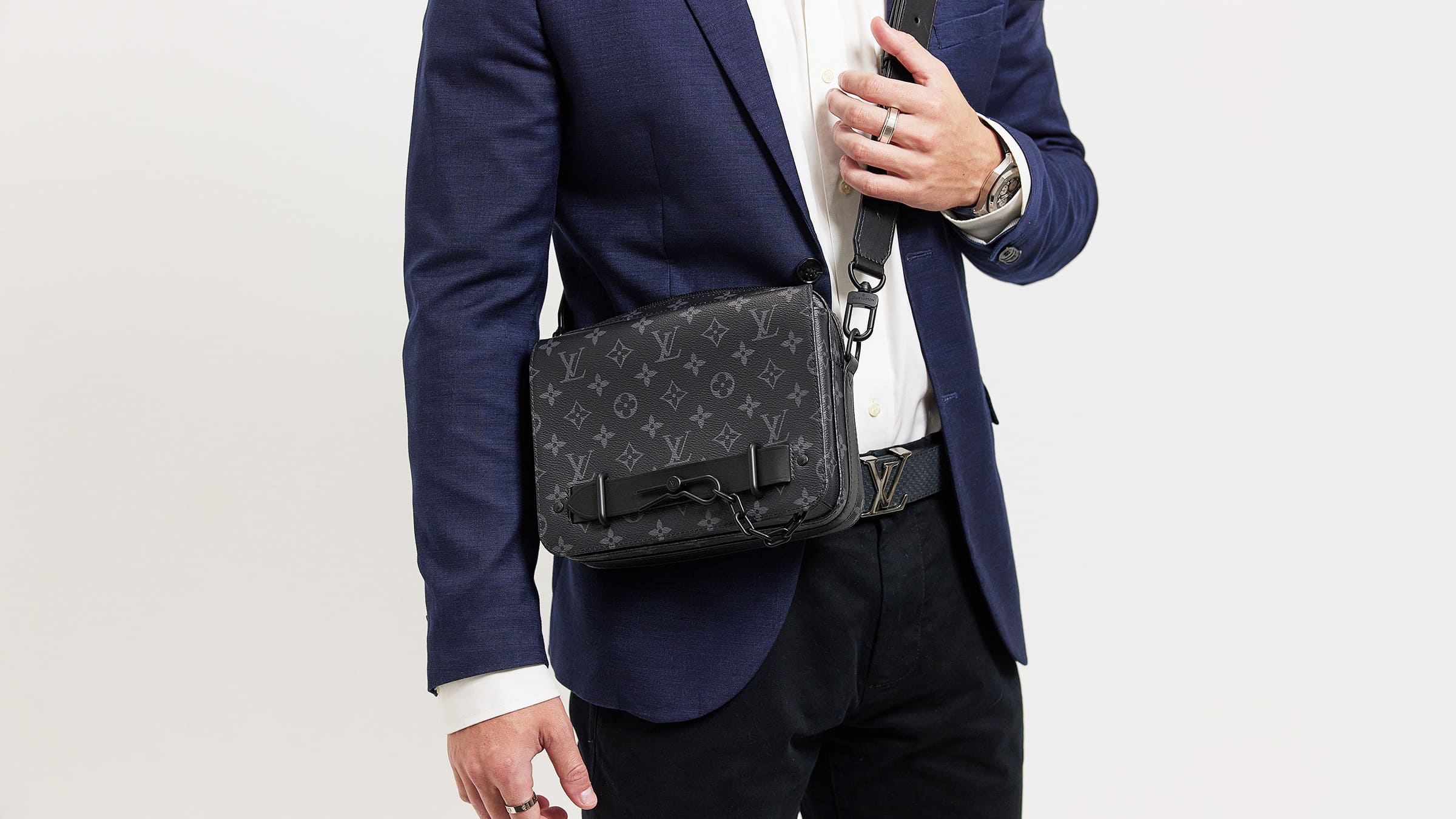 studio image of male model in a blue suit wearing a louis vuitton monogram trunk crossbody bag FASHIONPHILE
