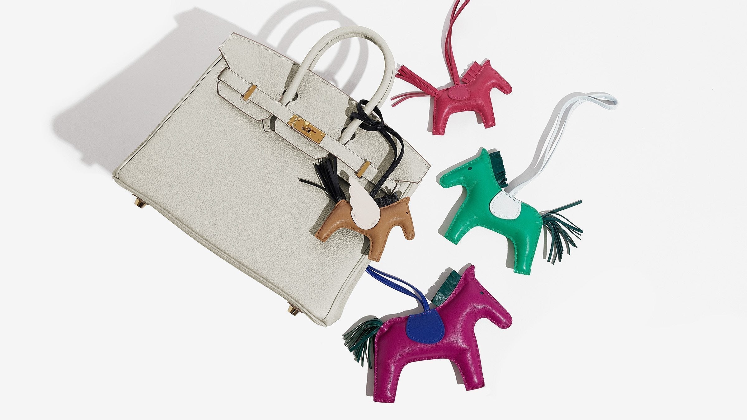 this is an image of hermes rodeo horse bag charm size comparisons next to a birkin bag for scale by fashionphile