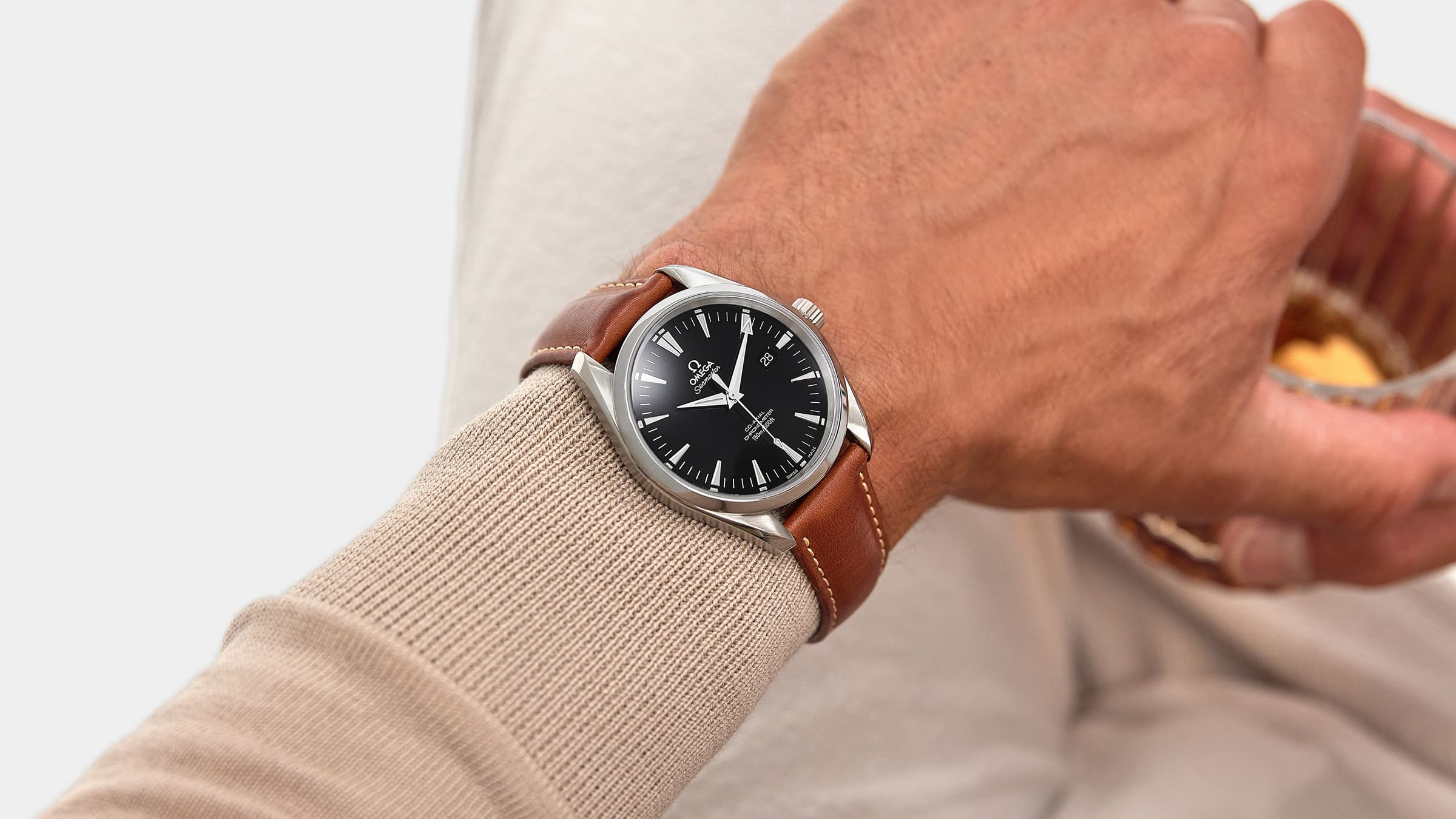 close up image of man wearing an omega seamaster watch with a brown leather bracelet and black dial by FASHIONPHILE