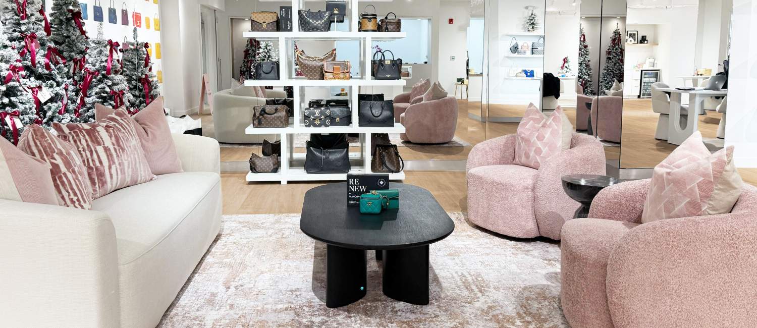 Luxury showroom with pink seating, a white display shelf of designer handbags, holiday décor, and mirrored walls